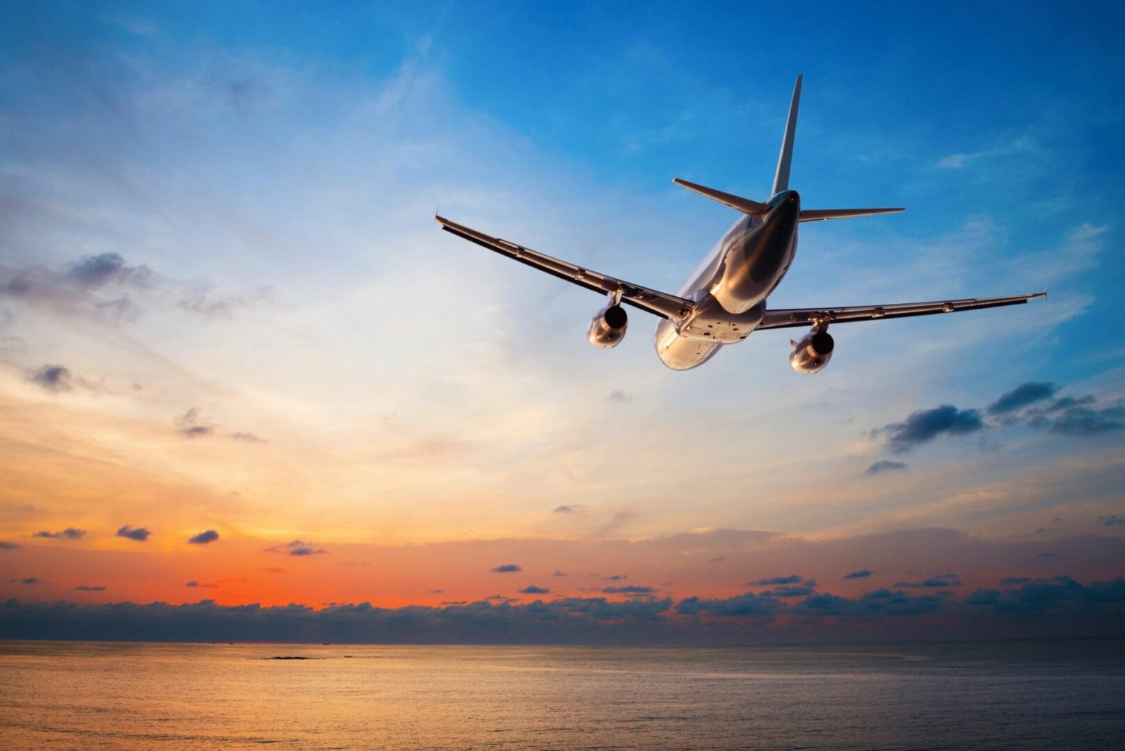 A plane flying over the ocean at sunset.