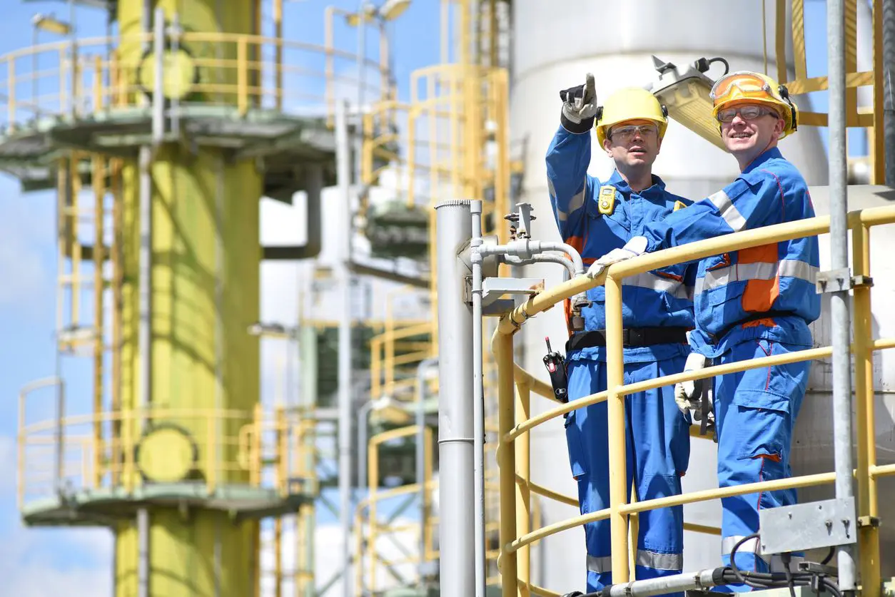 Two men in blue coveralls and hard hats standing on a platform.